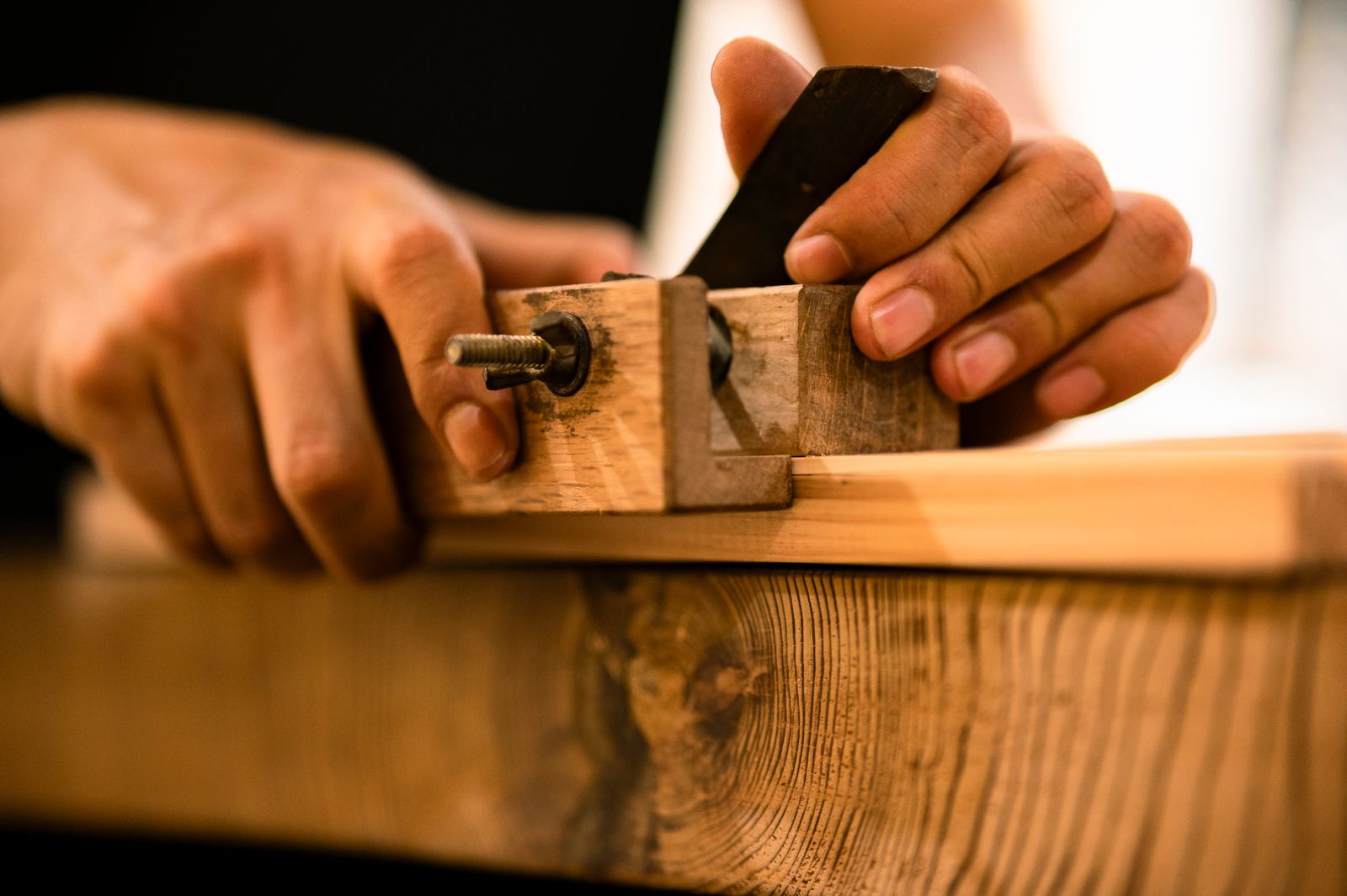 Hands guiding a wooden plane across a board